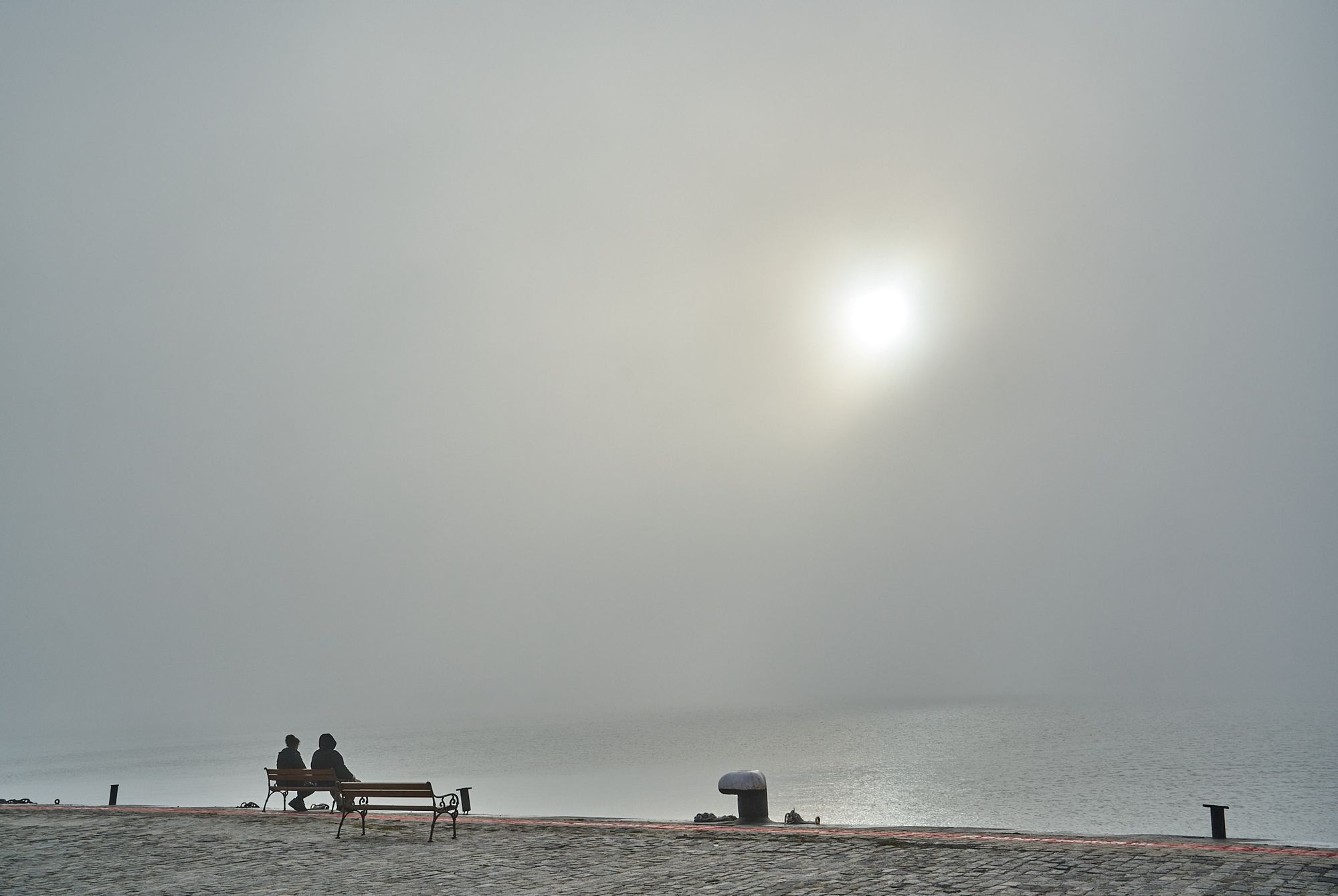 Two figures sitting on a bench at Port Varna in foggy weather