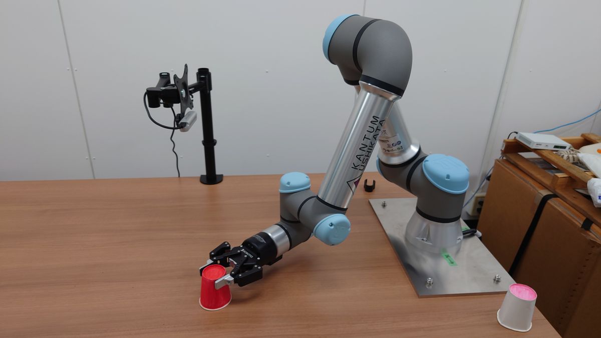 Universal Robotics社のUR5を使ったロボット実験の様子。上部に取り付けた3次元画像センサが物体（紙コップ）を見て、ロボットアームが掴んでいる。（2021年、早稲田大学・尾形研究室にて）