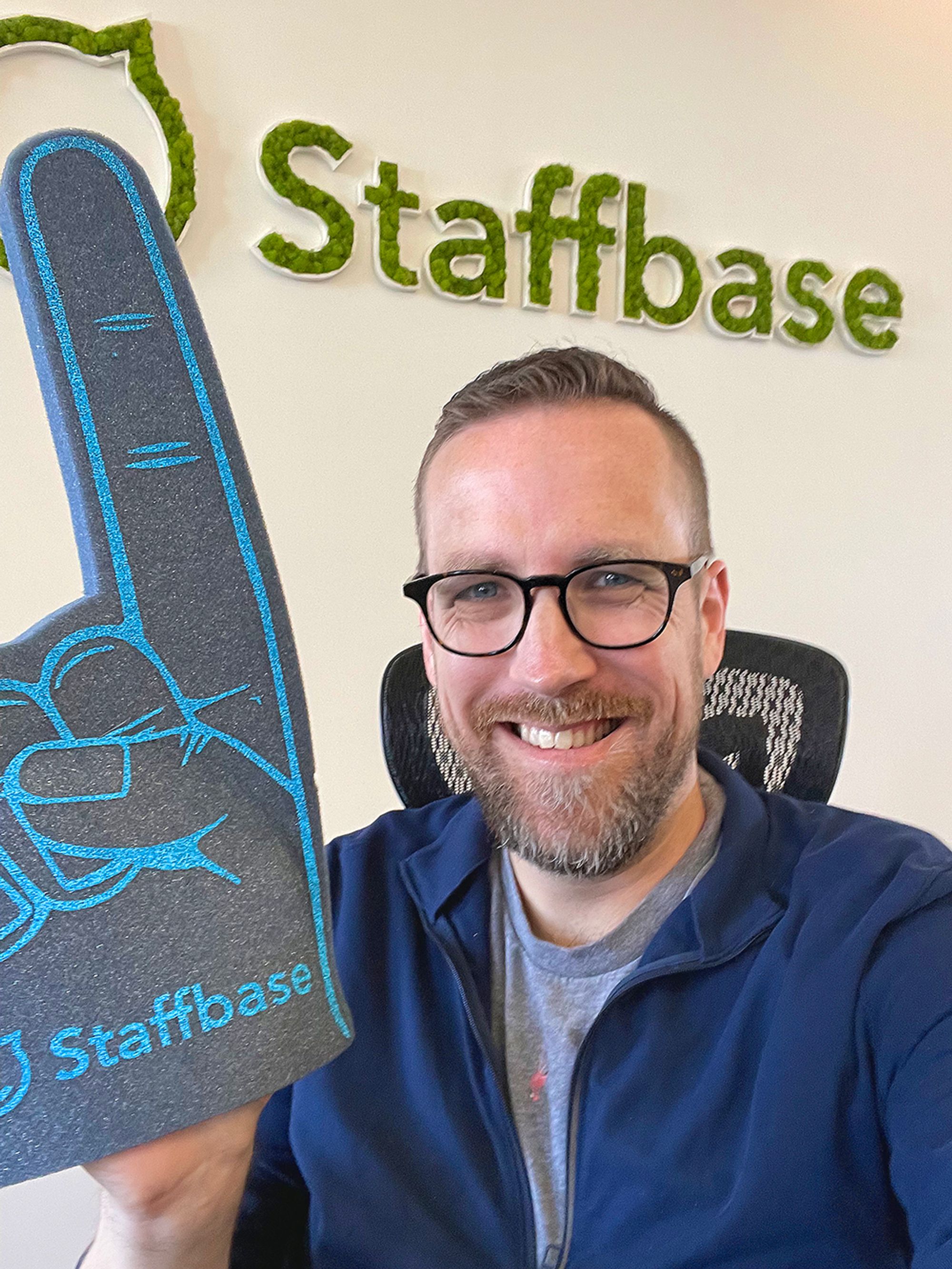 Photo of me with a Staffbase giant foam finger and the Staffbase logo on an office wall behind me