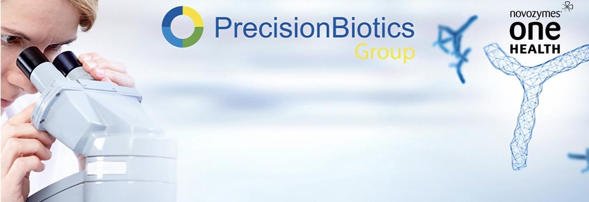 Figure 1: An image taken from the old PrecisionBiotics website. On the left is a young, blonde-haired man looking into a microscope. At the centre of the image is the old PrecisionBiotics logo. On the right side is the Novozymes One Health logo. In the background there are bacteria molecular structures.
